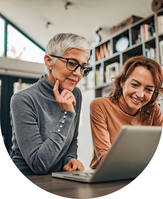 Two women smiling while using a laptop.